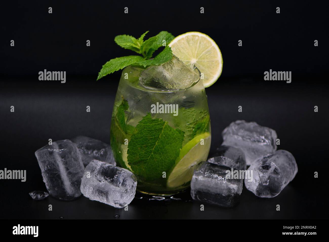 Cocktail mojito dans un verre rond, glacons, feuilles de menthe et rondelle de citron vert sur un fond noir, boisson rafraîchissante d'été Foto Stock