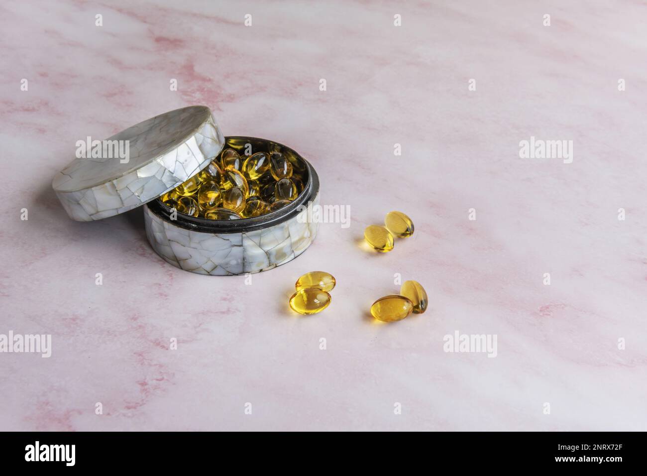 Un pillbox in madreperla con perle di integratori nutrizionali su sfondo di marmo rosa Foto Stock