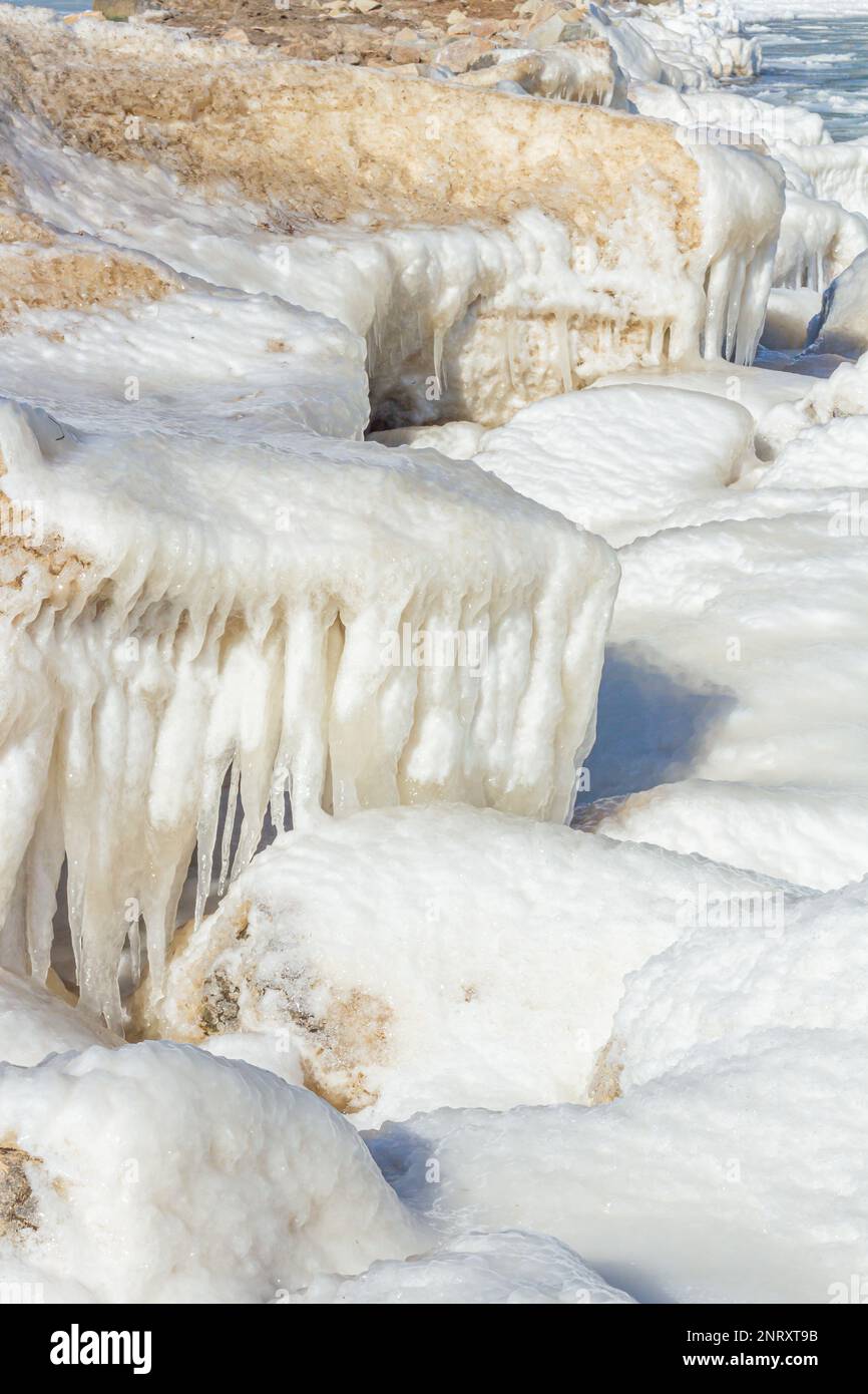 Primo piano della costa ghiacciata, delle onde ghiacciate, delle rocce e del sole che si abbagliano sul ghiaccio. Foto Stock