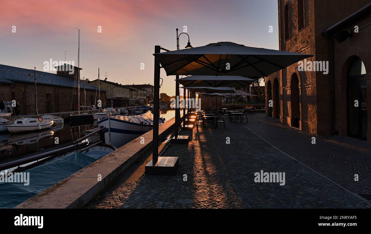 Il centro storico di Cervia al tramonto, il bacino di sale, il porto del canale, le barche ormeggiate, il magazzino di sale del 18th° secolo illuminato dalla calda risata Foto Stock