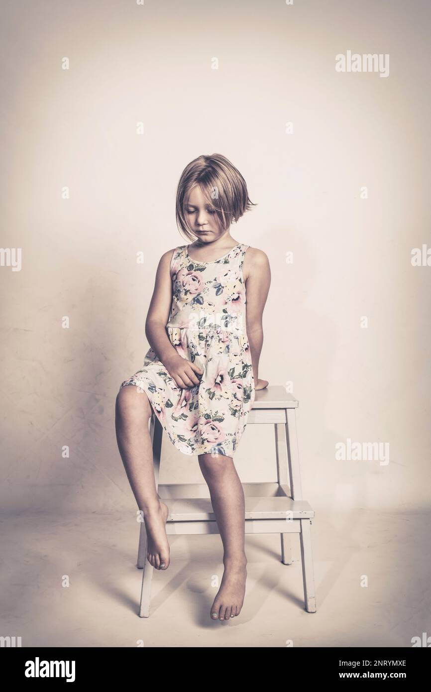 ragazza piccola triste si siede su uno sgabello che guarda il pavimento Foto Stock