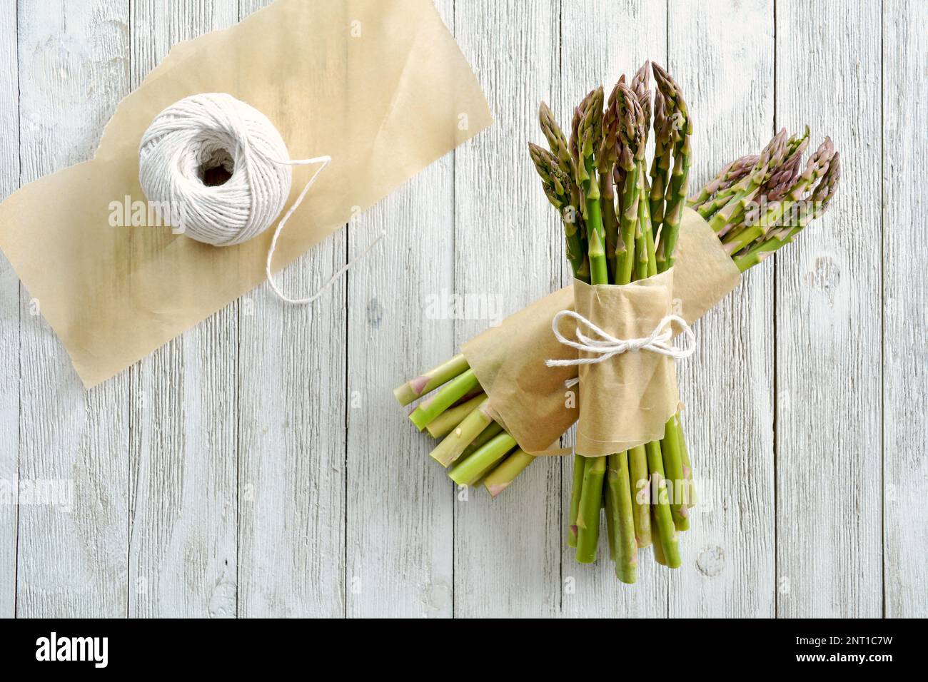 Asparagi freschi raccolti legati in grappoli con pergamena e filo di macelleria su fondo di legno grigio in composizione piana. Foto Stock