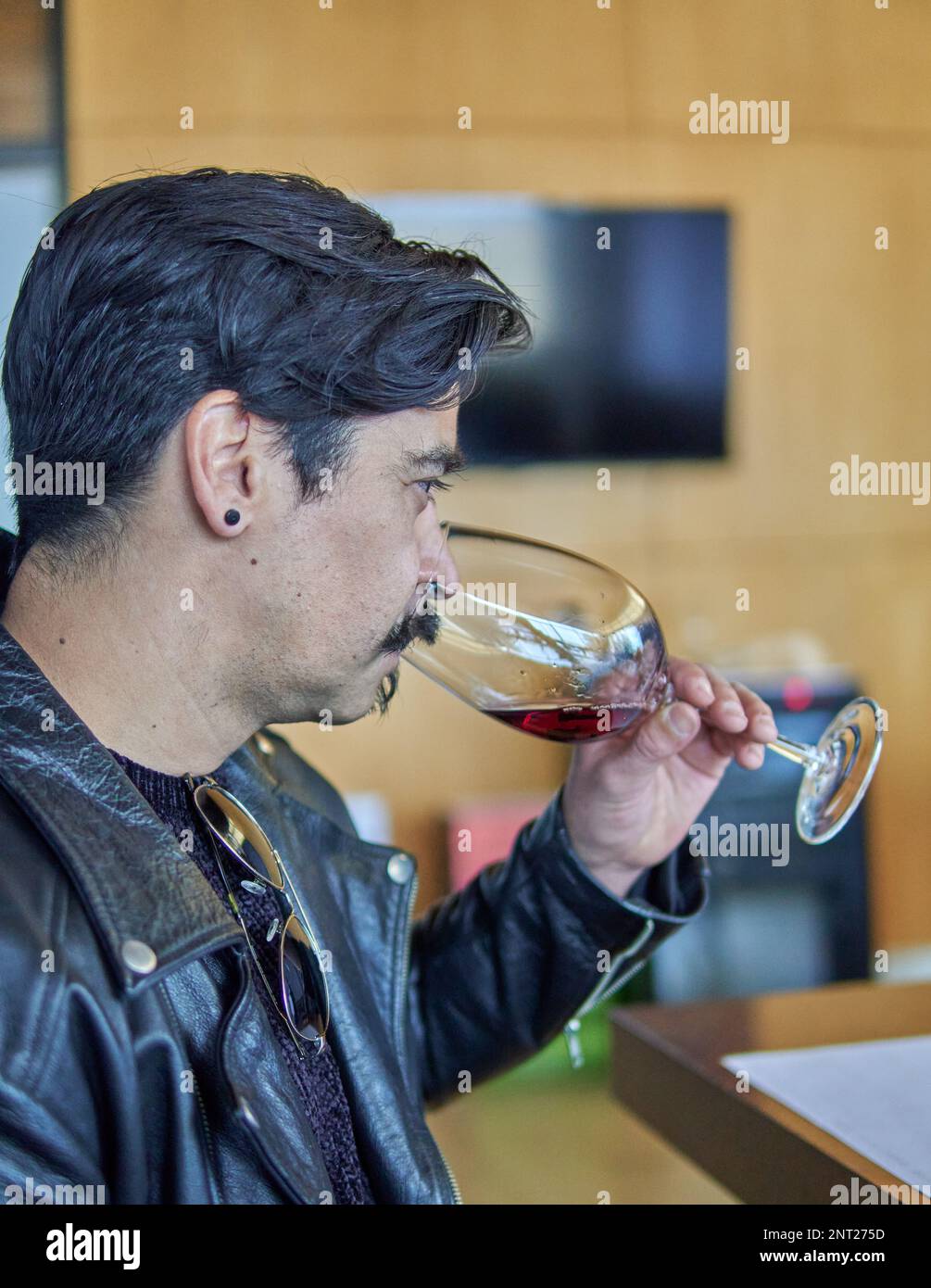 l'uomo latino in profilo ad una degustazione di vino in una cantina in mendoza argentina. Uomo brunetta in giacca di pelle con baffi che tiene e odora un bicchiere di Foto Stock