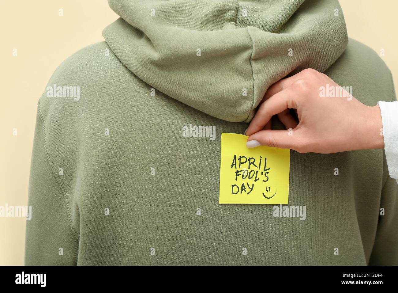 Donna che si attacca carta con testo APRILE FOOL's GIORNO sulla schiena dell'amico contro sfondo a colori, primo piano Foto Stock