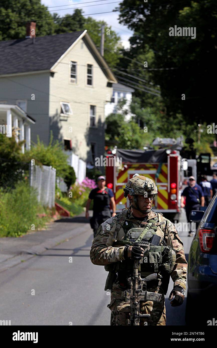 Members of the New Hampshire State Police SWAT team leave after Michael Burns was removed from the rear of his apartment building, left, in Claremont, N.H., on Thursday, Aug. 15, 2019. Police in New Hampshire detained Burns after a daylong standoff that started with reports of shots fired in the Claremont neighborhood. (Geoff Hansen/The Valley News via AP) Foto Stock