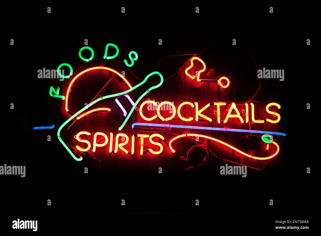 Una luce al neon modellata nella frase “Foods cocktails Spirits” con una bottiglia di champagne sul lato sinistro. Il bagliore del neon lascia apparire un mattone wa Foto Stock