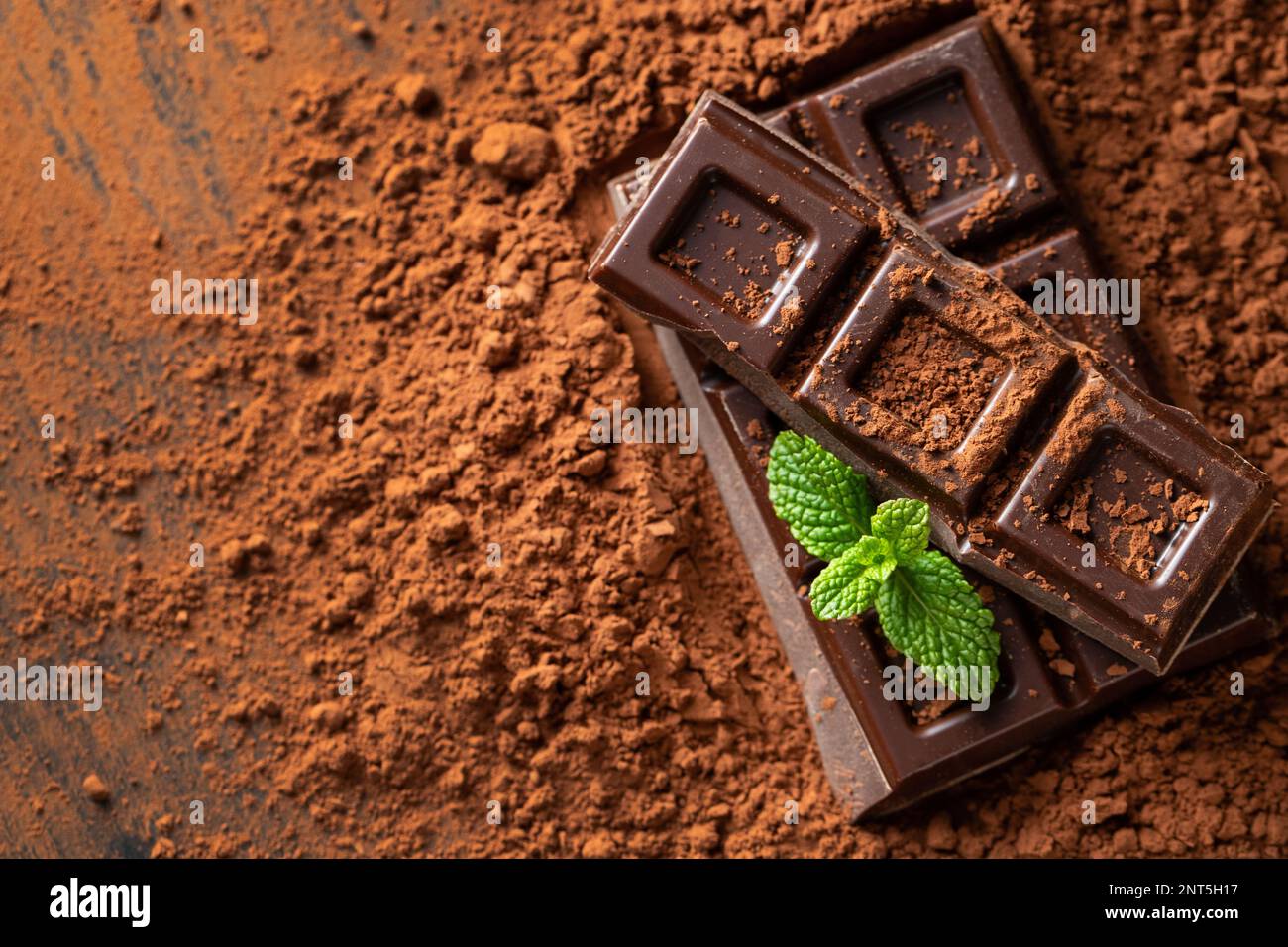 Cioccolato fondente e al latte con noci su fondo scuro cosparso di polvere di cacao. Pezzi di cioccolato con mandorle e nocciole primo piano. Vista dall'alto con Foto Stock