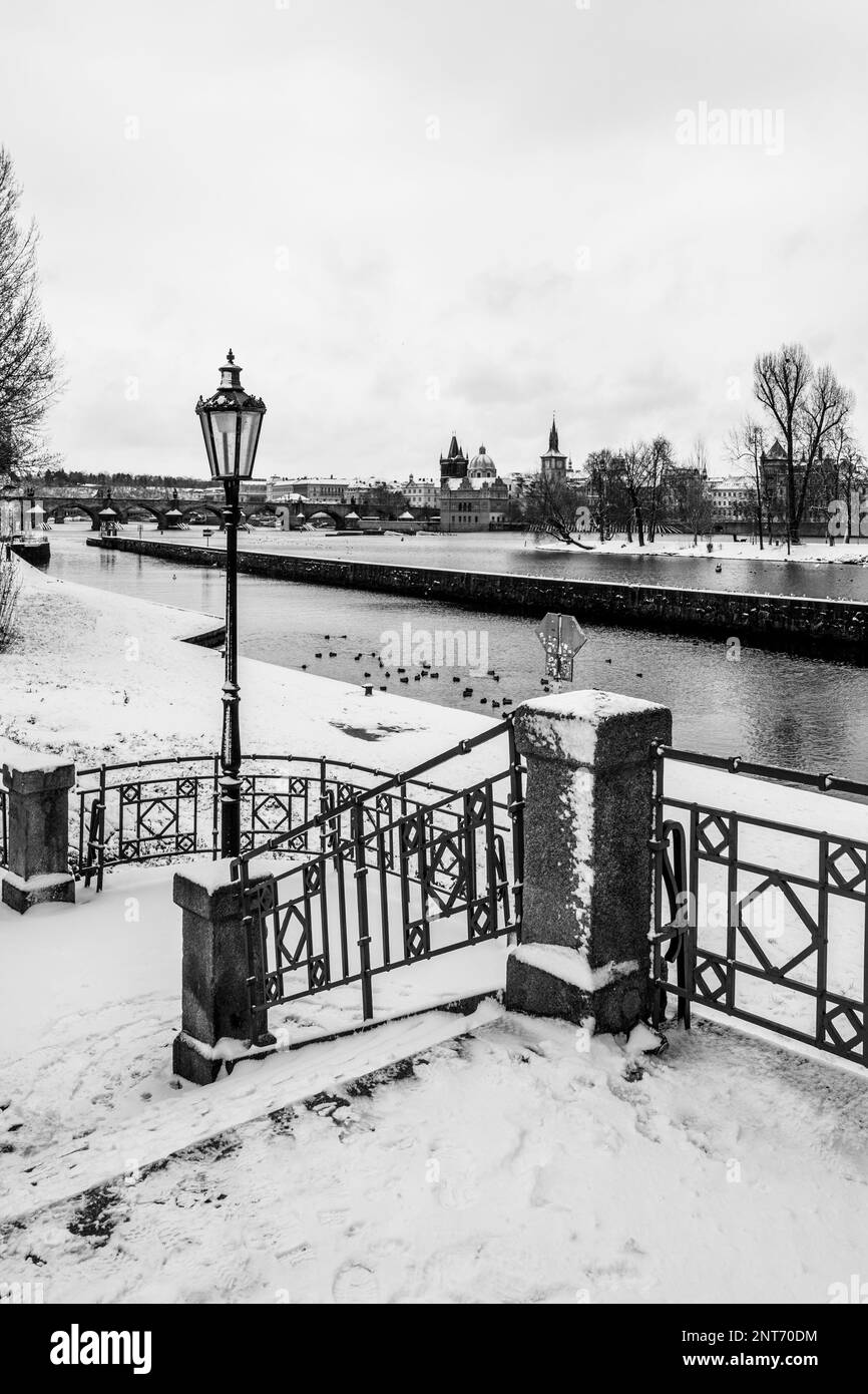 Scena invernale sulla riva del fiume Moldava a Praga. Presenta una scala che conduce verso il basso verso l'acqua, adornata da una ringhiera decorata e da una lampada storica. Sullo sfondo, si affaccia sul fiume e sul Ponte Carlo. Fotografia in bianco e nero. Foto Stock Scena invernale sulla riva del fiume Moldava a Praga. Presenta una scala che conduce verso il basso verso l'acqua, adornata da una ringhiera decorata e da una lampada storica. Sullo sfondo, si affaccia sul fiume e sul Ponte Carlo. Fotografia in bianco e nero. Foto Stock