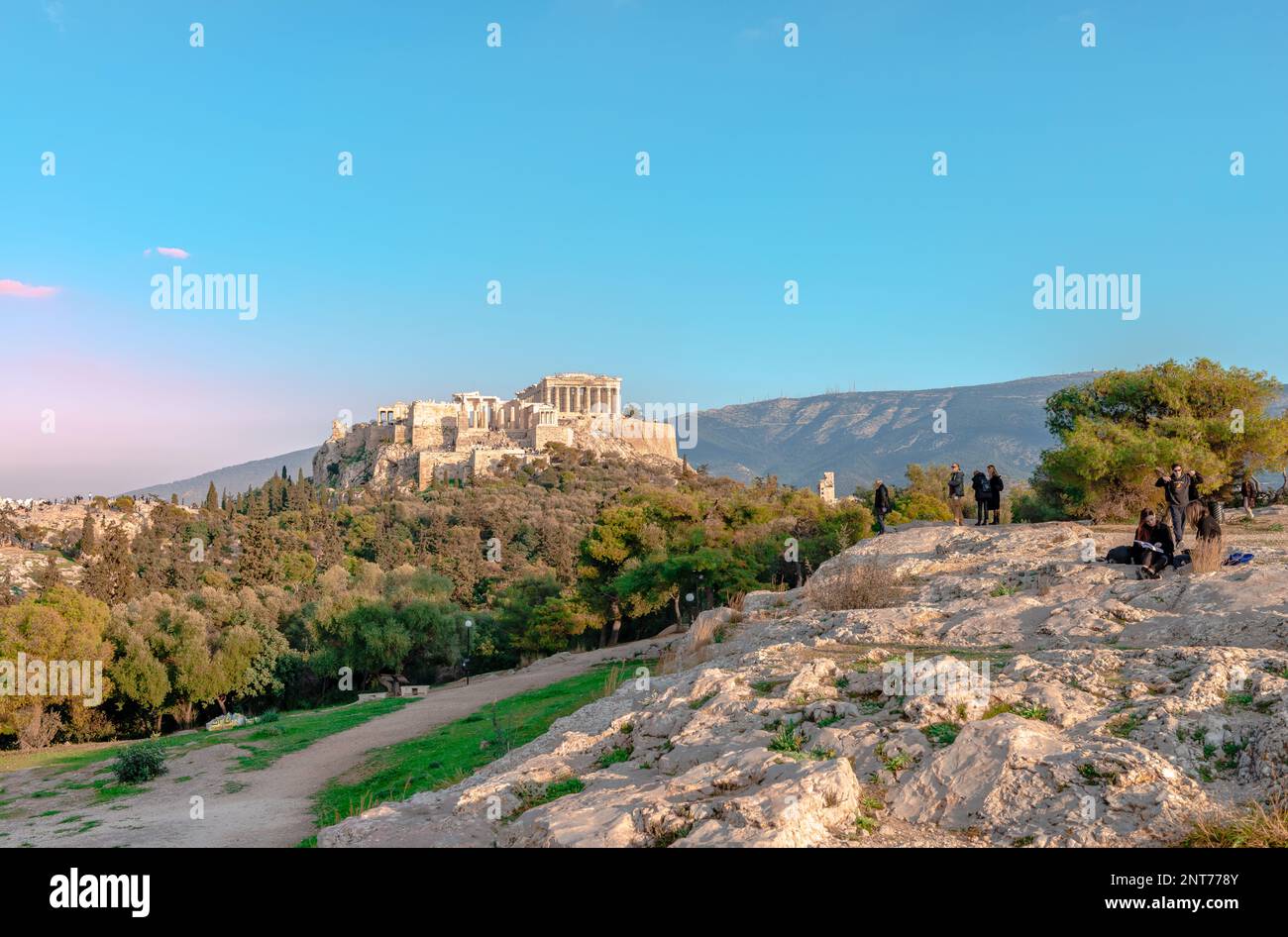 Gli incidentali sulla collina di Pnyx trascorrono un pomeriggio di sole, con l'Acropoli di Atene e la collina di Areopago sullo sfondo. Atene, Grecia. Foto Stock