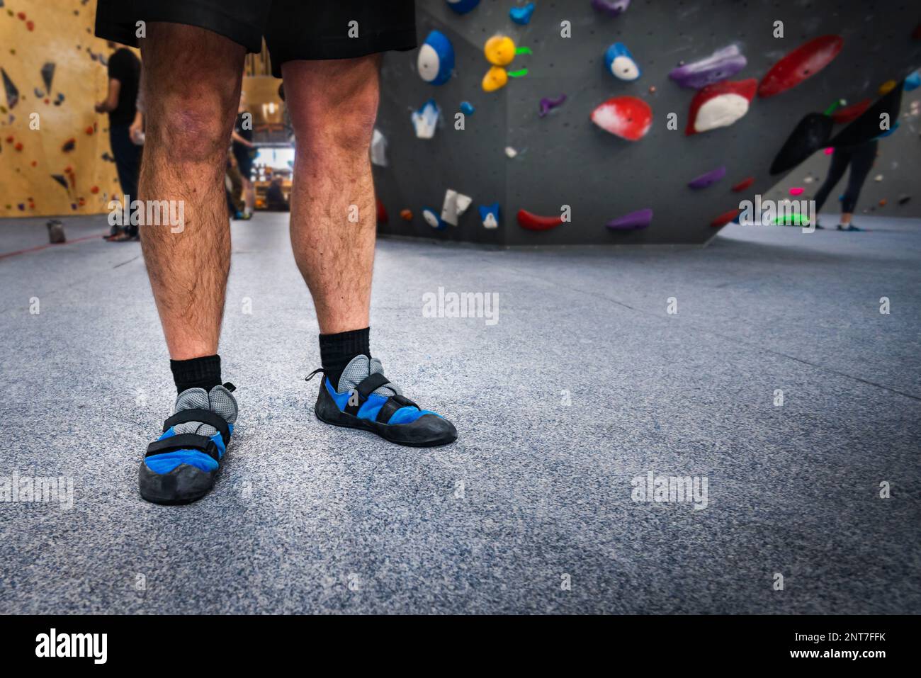 Arrampicatore maschio che indossa scarpe da parete per arrampicata indoor sui piedi, in piedi su un morbido tappetino di sicurezza per pavimenti. Foto Stock