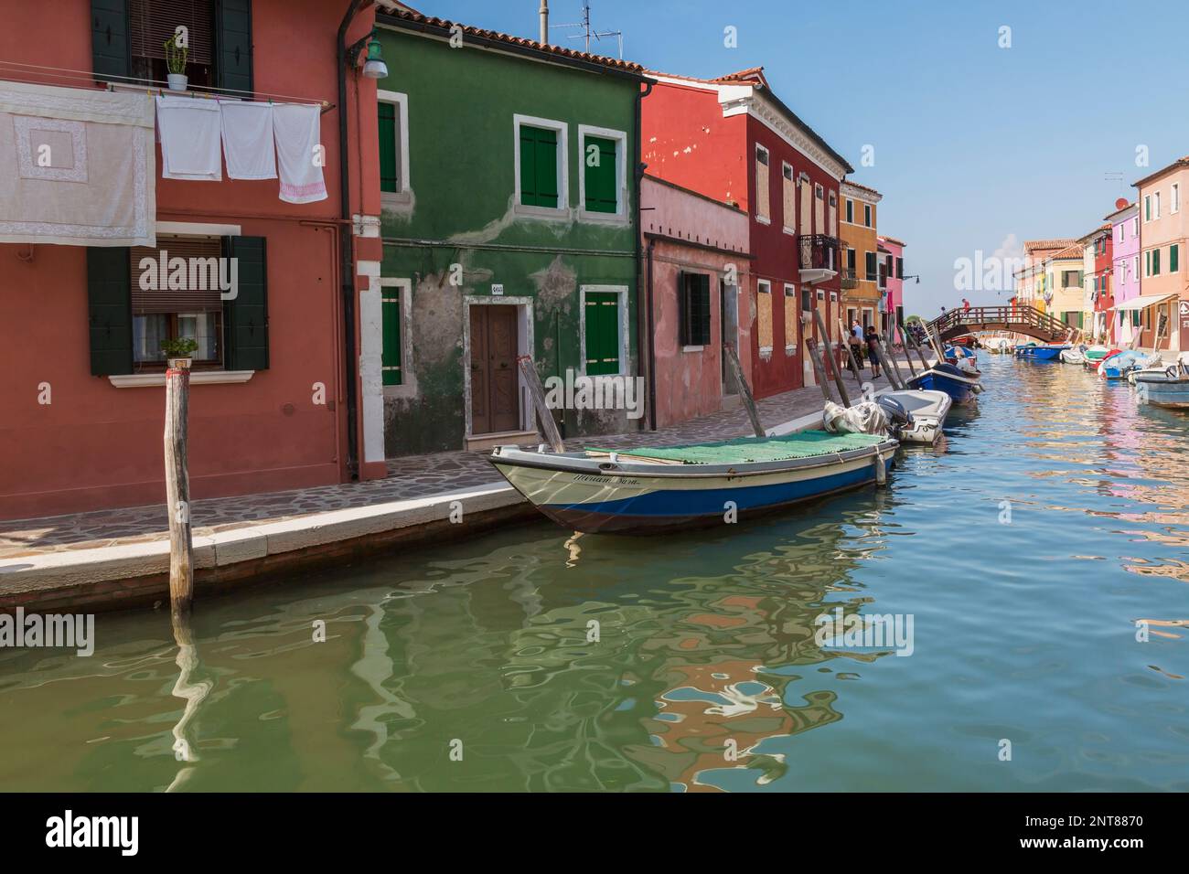 Barche ormeggiate sul canale fiancheggiato da case colorate e negozi più passerella in legno, Isola di Burano, Laguna di Venezia, Venezia, Veneto, Italia. Foto Stock