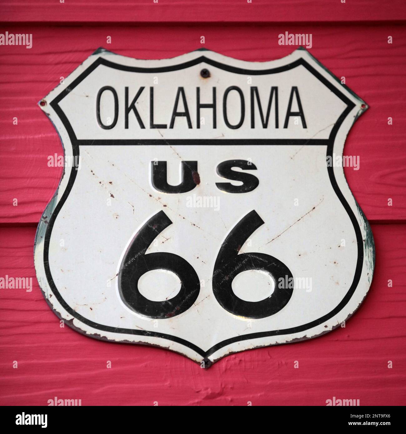 Primo piano su un cartello stradale dell'Oklahoma US 66 avvitato su una parete di legno dipinta di rosso. Foto Stock