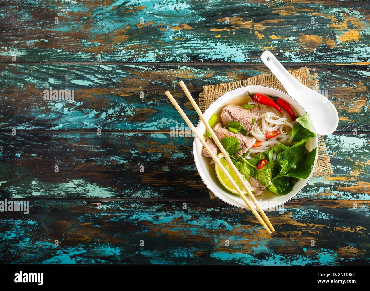 Tradizionale zuppa vietnamita Pho bo con erbe aromatiche, di carne o di riso tagliatelle, brodo. Pho bo nella ciotola con bacchette, cucchiaio. Spazio per il testo. Vista dall'alto. Zuppa asiatica Foto Stock