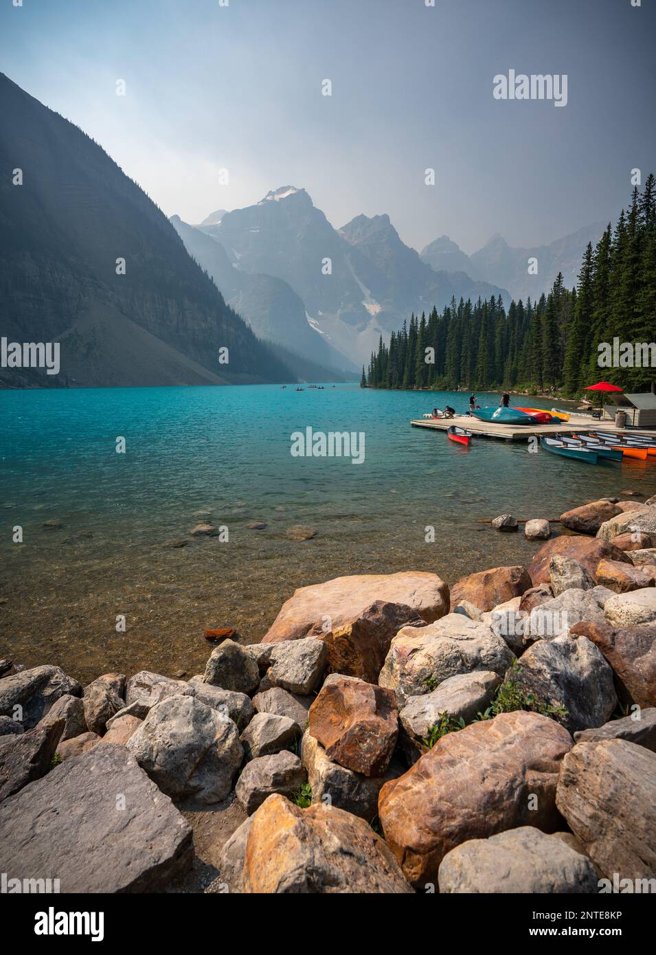 Lago Moraine con catena montuosa dai cieli nebbiosi e acque acquatiche Foto Stock