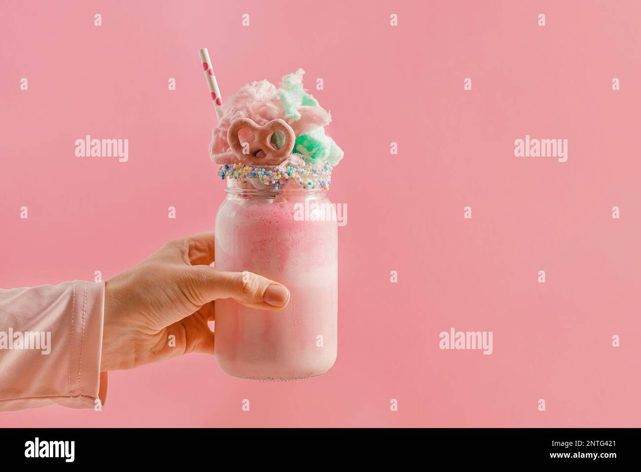 Mano femminile che tiene in mano un vaso di vetro con un milkshake di fragole sormontato da caramelle di cotone Foto Stock
