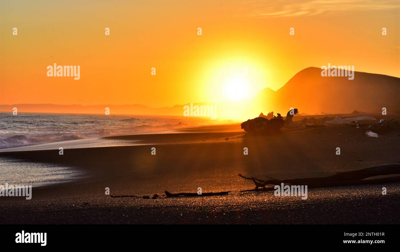 Bagliore arancione di un sole che tramonta su una spiaggia solita della Nuova Zelanda. Foto Stock