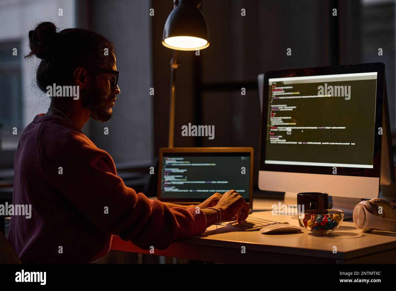 Giovane programmatore seduto al suo posto di lavoro e lavorando al computer con codici, lavora in ufficio fino a tarda notte Foto Stock