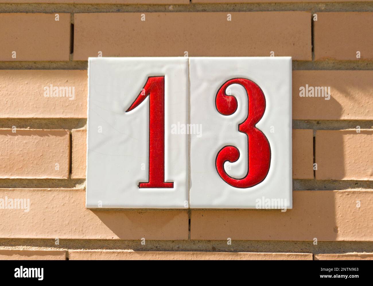 Casa numero 13 su muro di mattoni soleggiato. Case con concetto di personalità Foto Stock