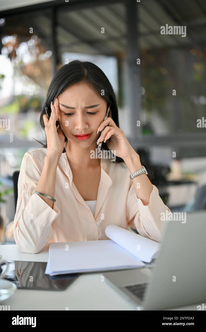 Seria e stressata donna d'affari asiatica o manager femminile è al telefono con qualcuno, avendo una seria telefonata, confuso e sconvolto. Foto Stock