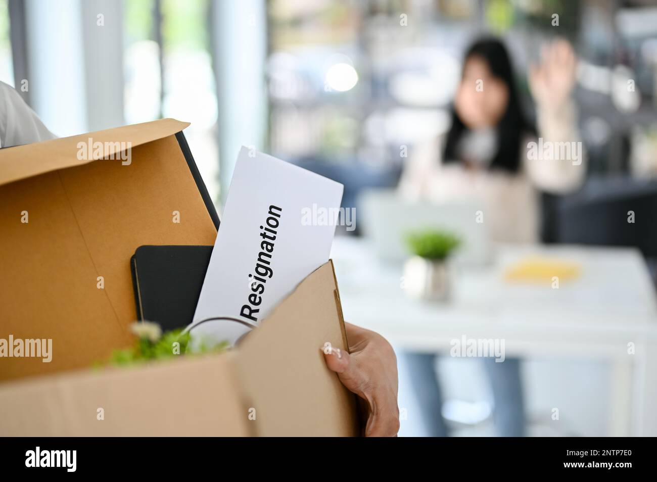 Immagine ravvicinata di una scatola di cartone con una lettera di dimissioni e materiale personale sullo sfondo sfocato dell'ufficio. disoccupazione, dimissioni, fallimento della carriera, m Foto Stock