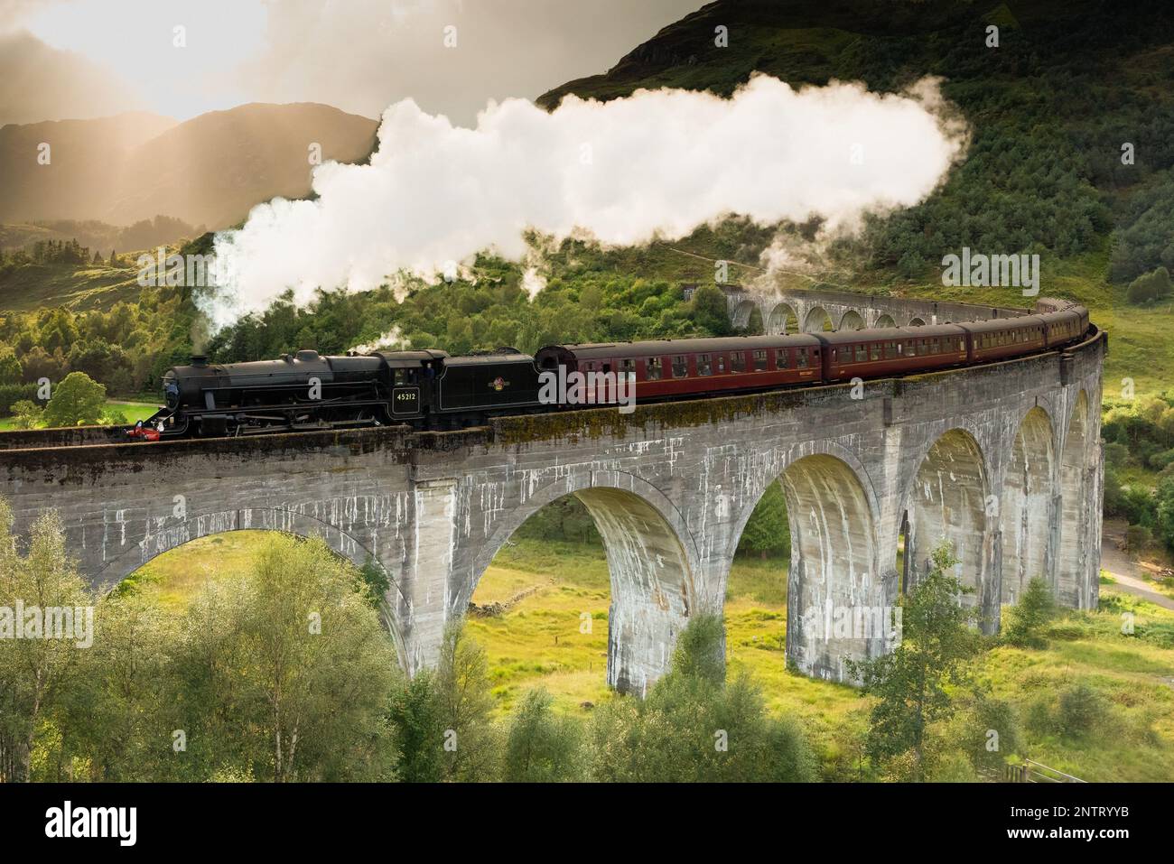 Treno a vapore Jacobite passando sopra il Viadotto Glenfinnan reso famoso dai film di Harry Potter. Situato nella valle con le montagne in Scozia Foto Stock