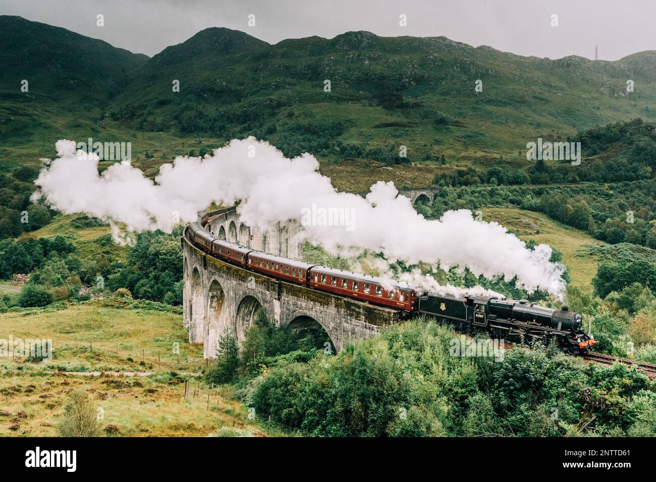 Treno a vapore Jacobite passando sopra il Viadotto Glenfinnan reso famoso dai film di Harry Potter. Situato nella valle con le montagne in Scozia Foto Stock