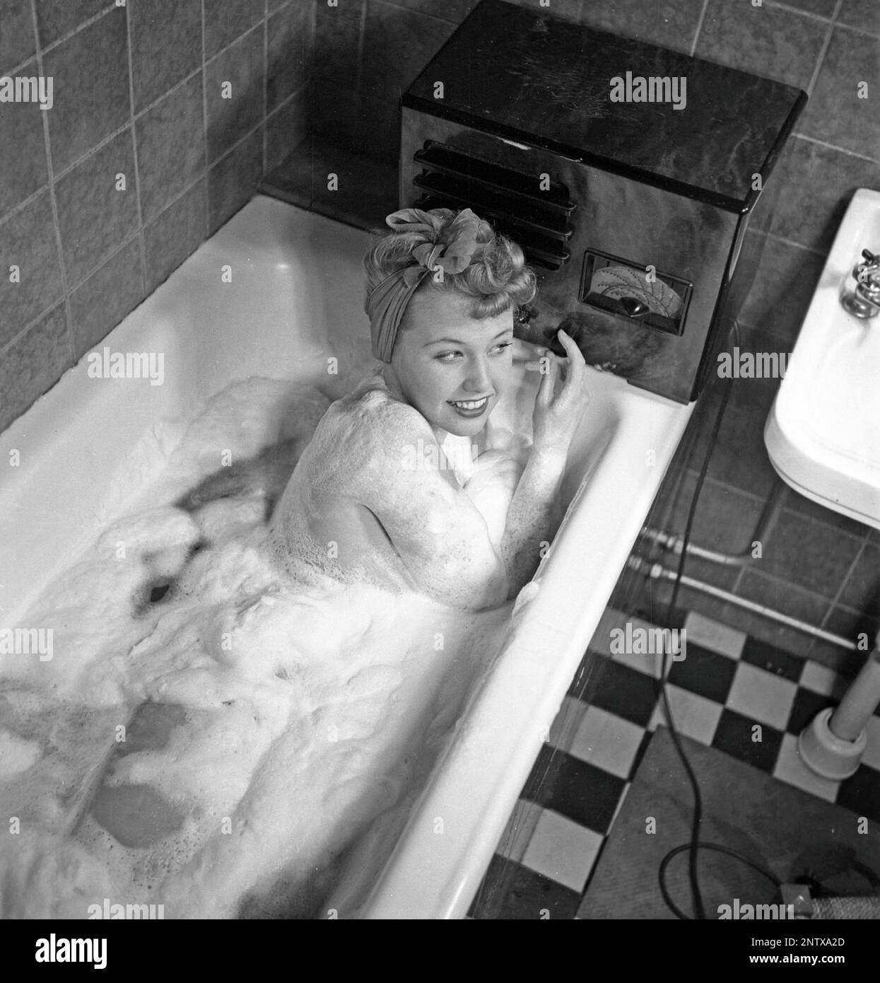 Ascoltatori radio in passato. Una giovane donna nella vasca da bagno che si affaccia alla radio che si siede sul bordo della vasca. Sulla parte anteriore della radio è presente una scala e quando si ruota la manopola accanto ad essa in modo che il puntatore si trovi al centro del nome di una stazione, la stazione era lì. Oltre alle trasmissioni FM, hanno anche ascoltato le radio straniere a onde lunghe. Svezia nel 1945 Kristofferson Ref L180-4,2 Foto Stock