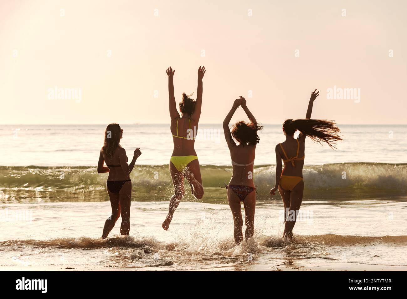 Quattro ragazze giovani felici e sottili stanno divertendosi e ballando al tramonto sulla spiaggia di mare Foto Stock