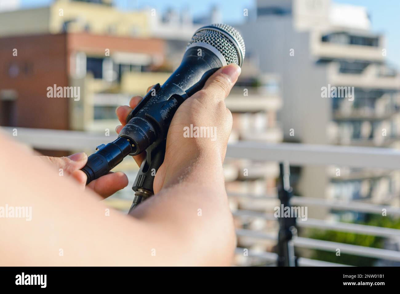 mani maschili irriconoscibili che installano il cavo audio su un microfono su un'asta di supporto, su un set di recital dal vivo, all'aperto. Foto Stock