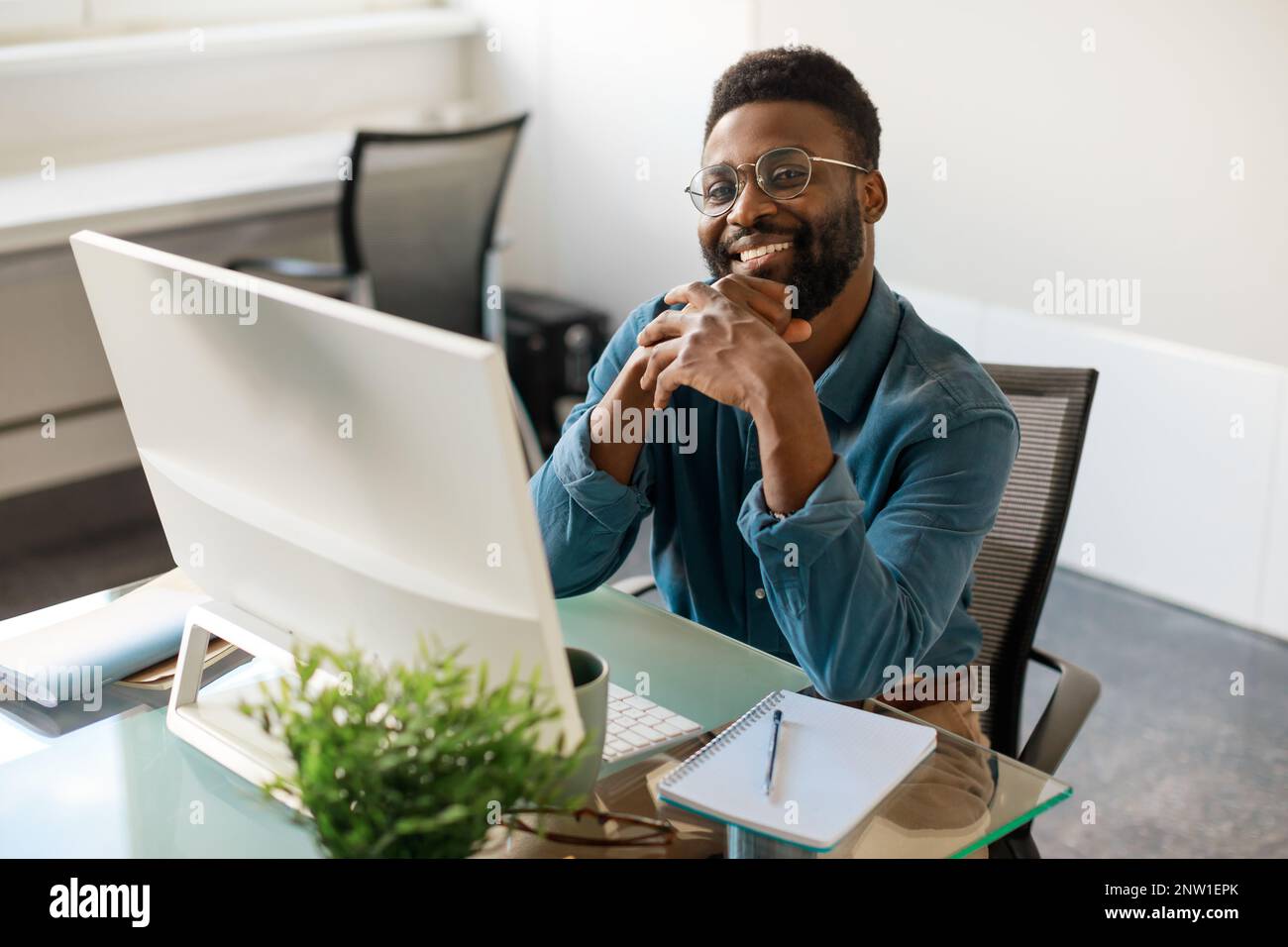 Buon uomo d'affari o CEO afroamericano seduto alla scrivania di fronte al computer, sorridente alla fotocamera, spazio libero Foto Stock