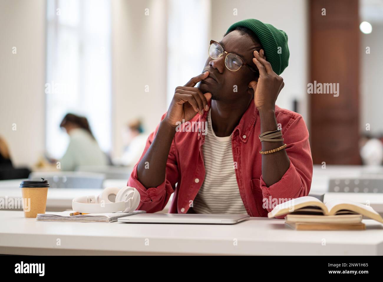 Un ragazzo afroamericano perplesso ha perso nei pensieri mentre studiava nella biblioteca dell'università Foto Stock