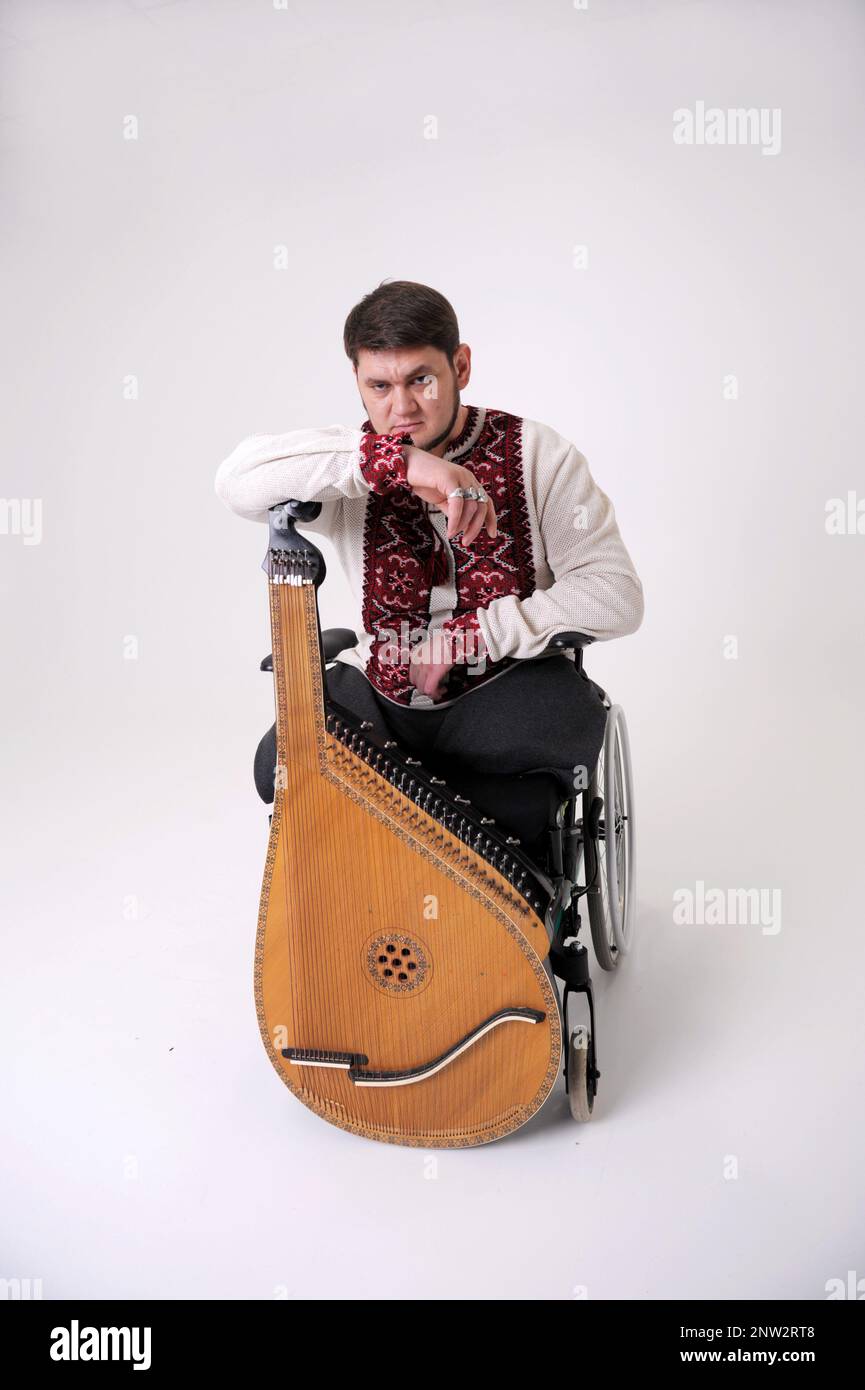 Cossack ucraino appoggiato su un musicista bandura su uno sfondo bianco in una sedia a rotelle bella musica intrattenimento interessi camicia ricamata su uno sfondo bianco rosso a croce-punto Foto Stock