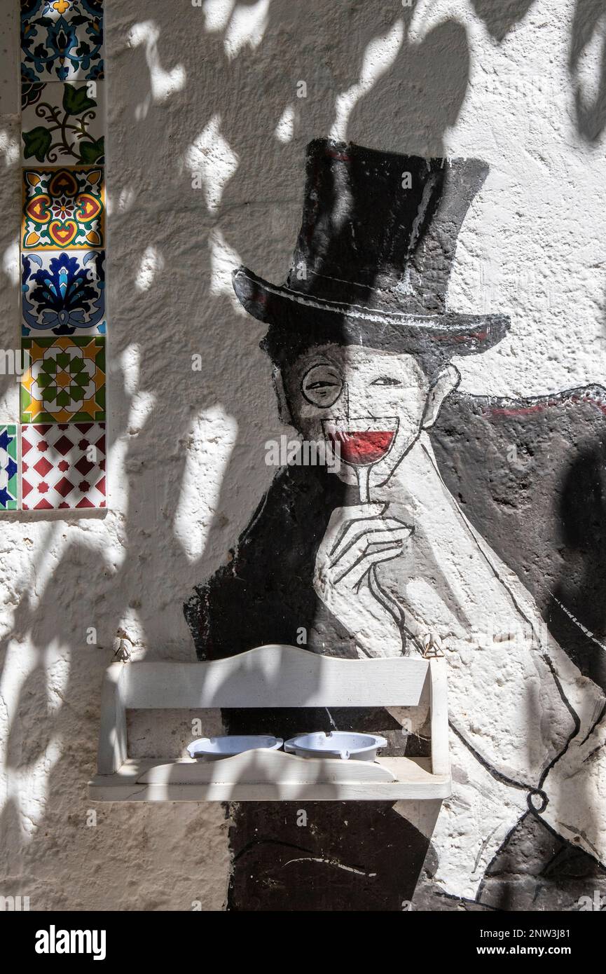 Street art di un uomo con un cappello che sorregge un bicchiere di vino rosso in una tranquilla strada di Grottaglie, Puglia, Italia Foto Stock