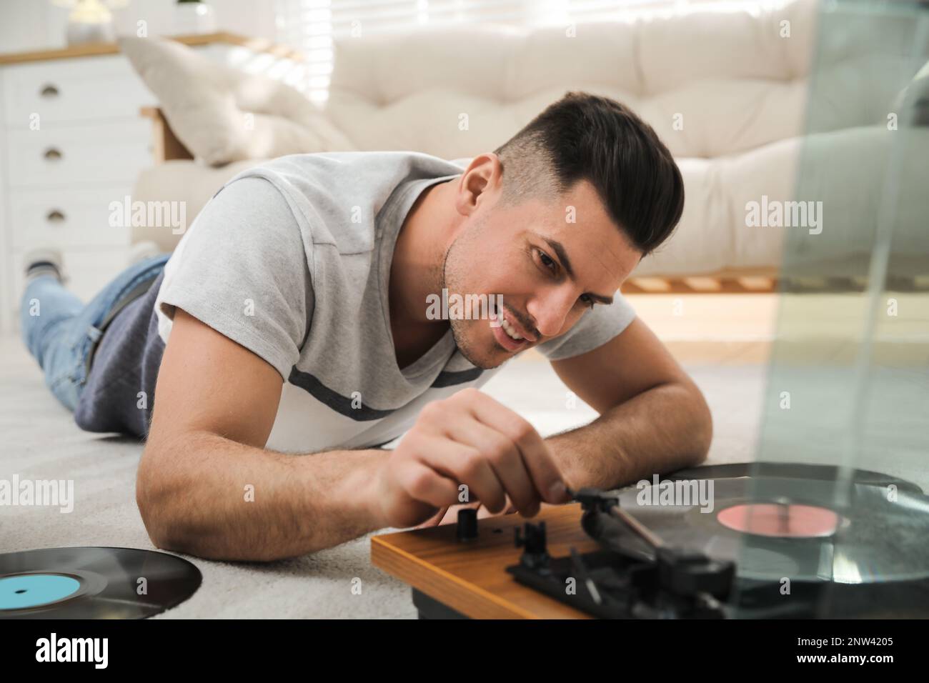 Uomo felice che usa il giradischi mentre si sdraiava sul pavimento a casa Foto Stock