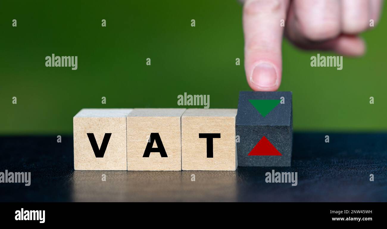 Simbolo per la riduzione dell'imposta sul valore aggiunto (IVA). La mano gira il cubo di legno e cambia il simbolo da alto a basso. Foto Stock