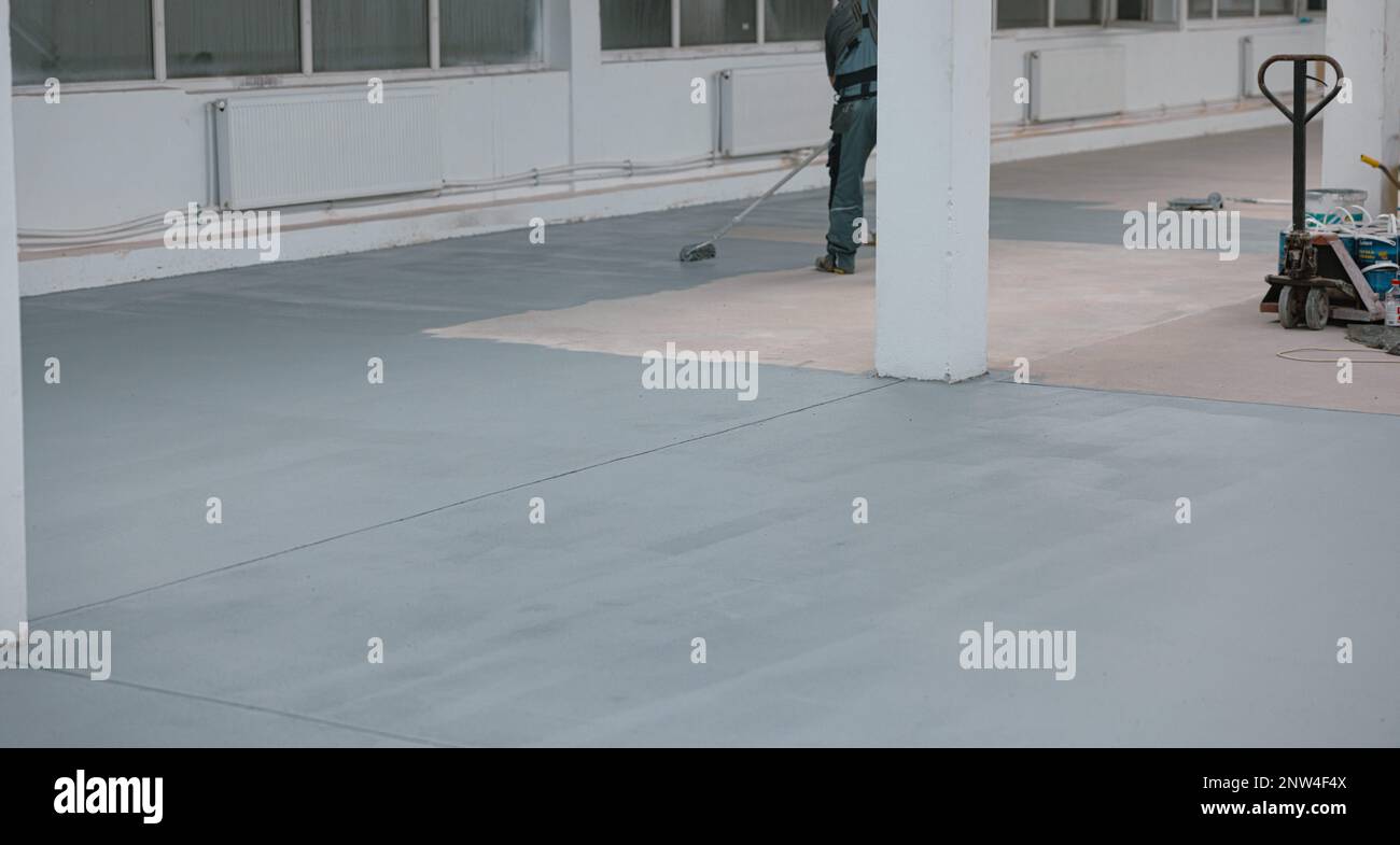 Lavoratore dipinge il pavimento di calcestruzzo con vernice grigia liquida Foto Stock