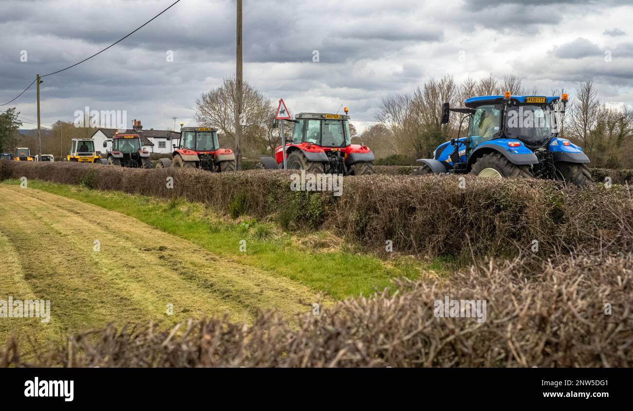 Una processione di trattori moderni si fa strada lungo una corsia di campagna a Wisborough Green, West Sussex, Regno Unito. Foto Stock