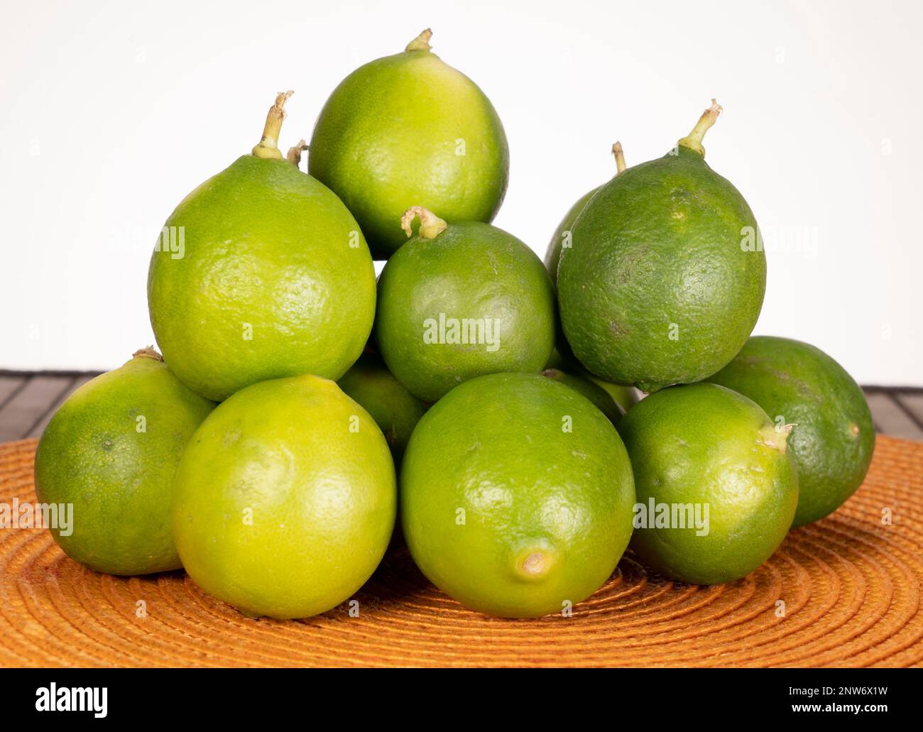 Limoni freschi interi disposti a piramide su una tovaglietta tessuta arancione su sfondo bianco, primo piano di agrumi. Foto Stock