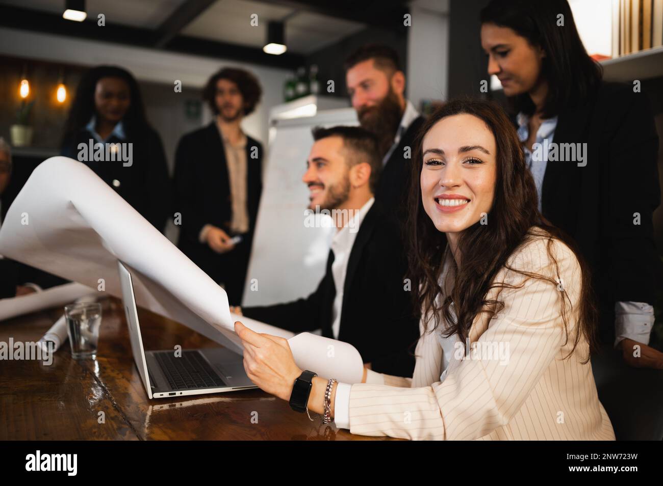ritratto di giovane donna sorridente alla macchina fotografica che tiene un foglio o un blueprint. Uomini d'affari che hanno una riunione di lavoro. Foto Stock
