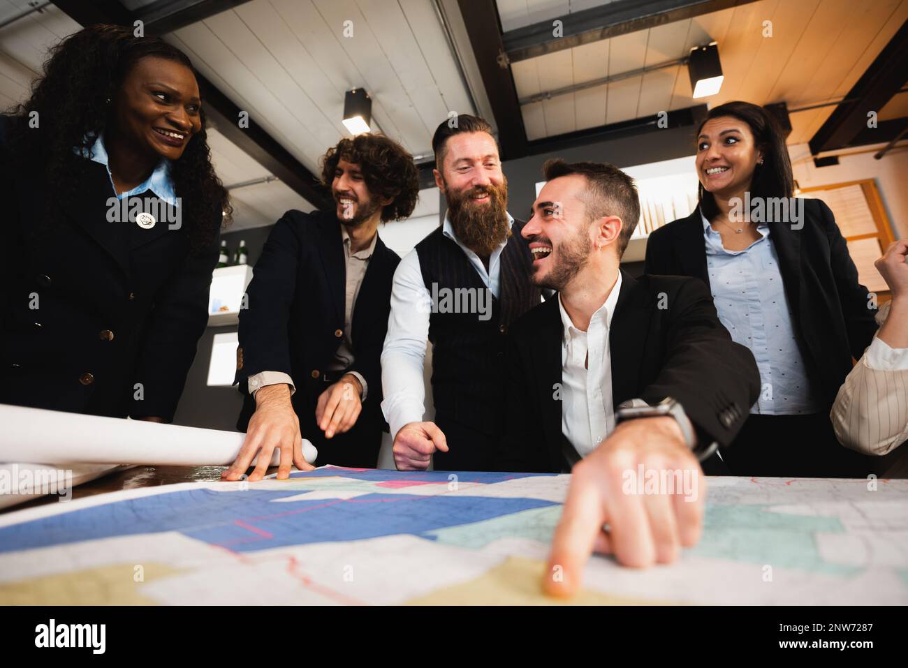 Lavoro di squadra felice con etnia diversa godendo di lavorare insieme. POV maschio puntando qualcosa su Blueprints sulla scrivania. Foto Stock