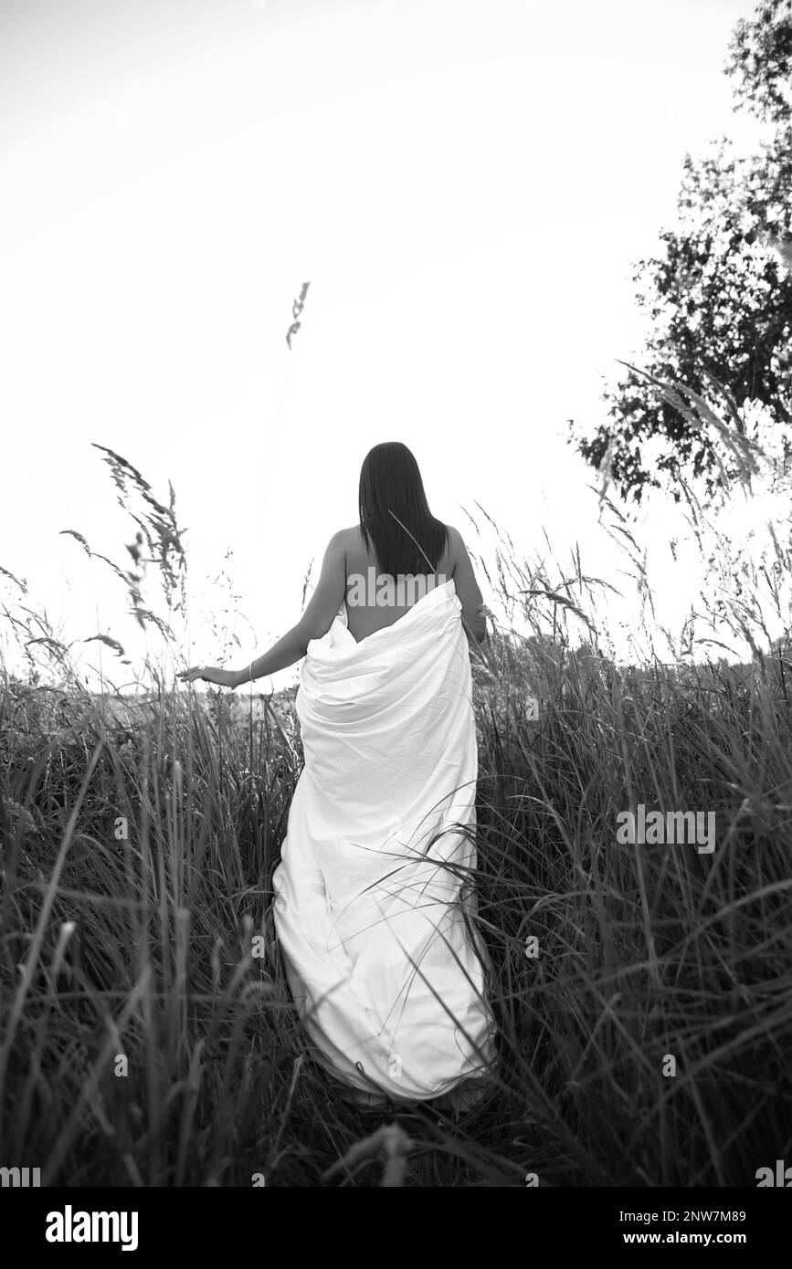 Foto in bianco e nero di una bella donna in un vestito bianco in piedi sull'erba. Foto Stock