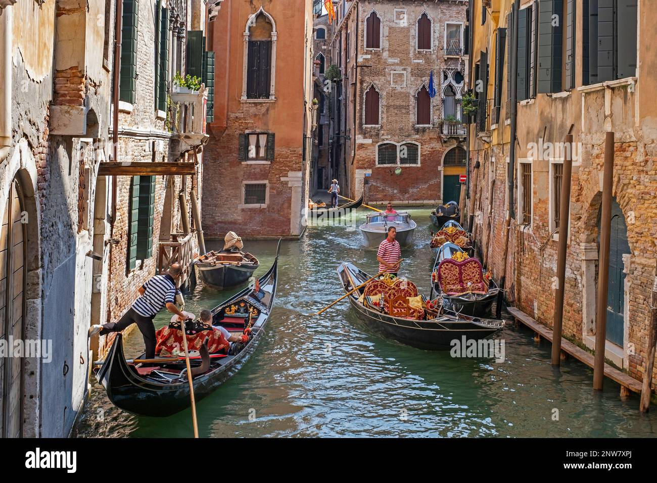 Gondolieri in gondole tradizionali che prendono i turisti in giro turistico lungo i canali stretti a Venezia, Veneto, Italia nordorientale Foto Stock