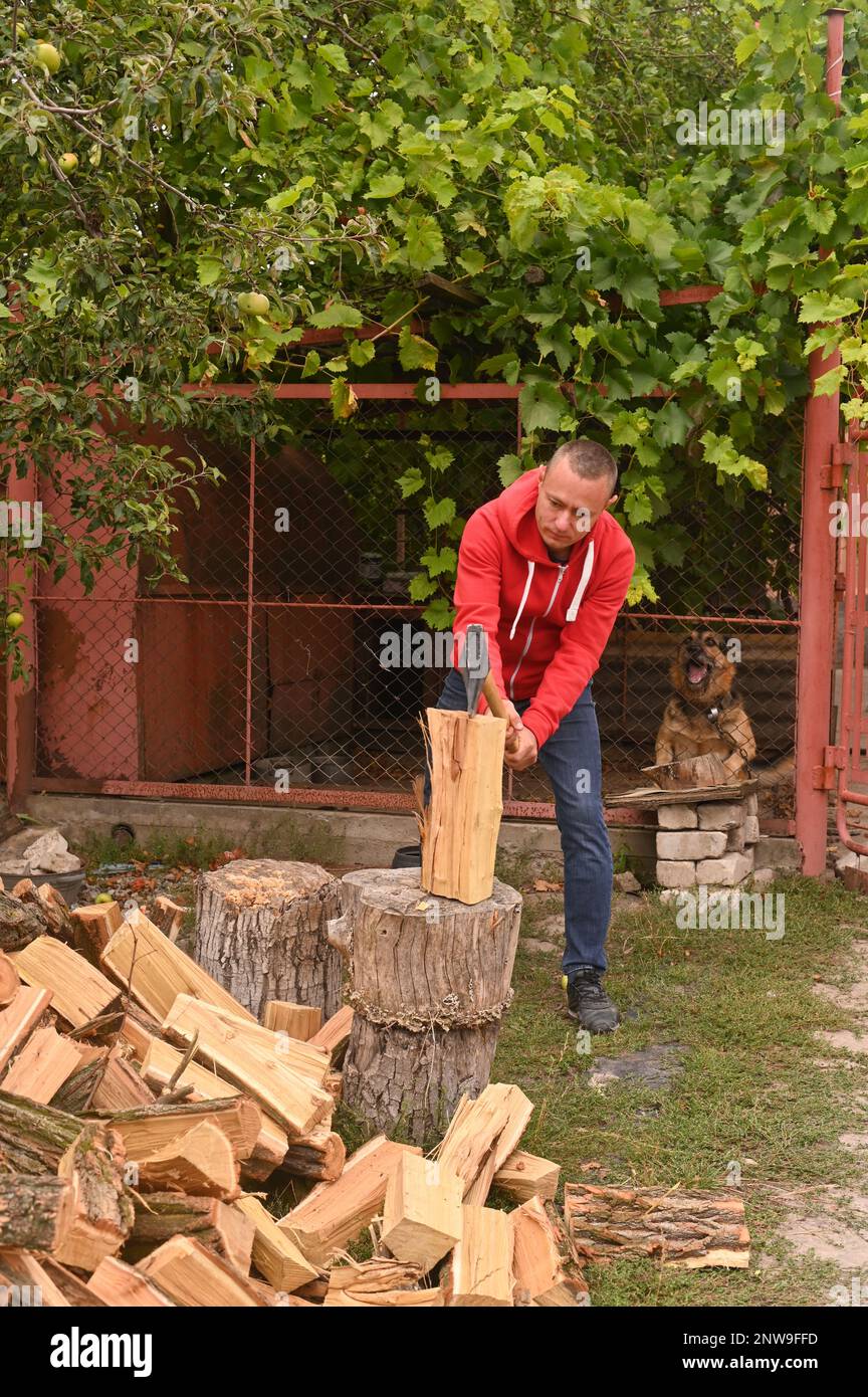 Un uomo con un'ascia sta tritando la legna sulla strada di fronte alla casa. foto verticale Foto Stock