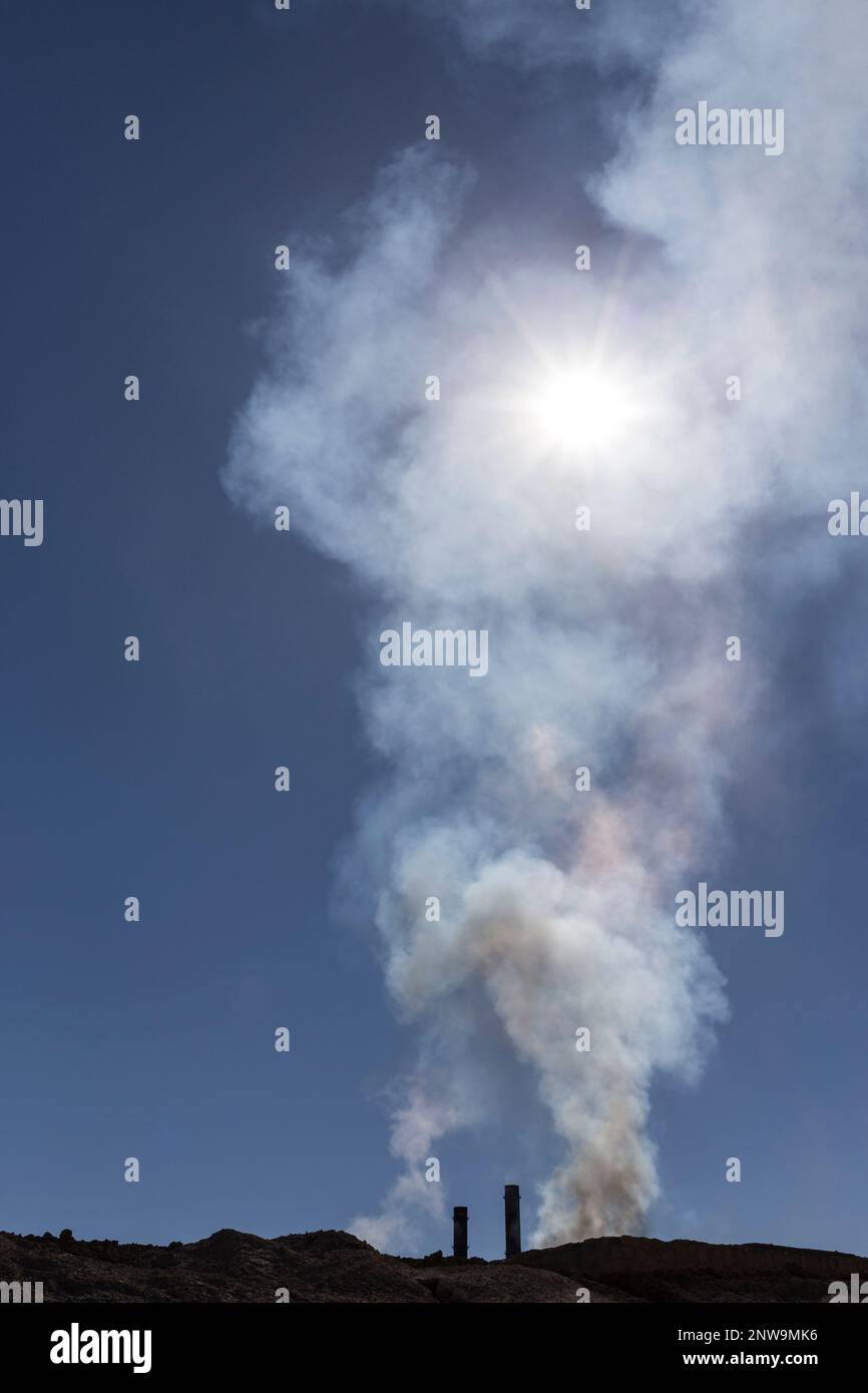 Complesso minerario industriale su terreni aridi che rilasciano fumi tossici nel cielo blu. Fonderia mineraria che spewing inquinanti nell'aria durante una giornata di sole vertic Foto Stock