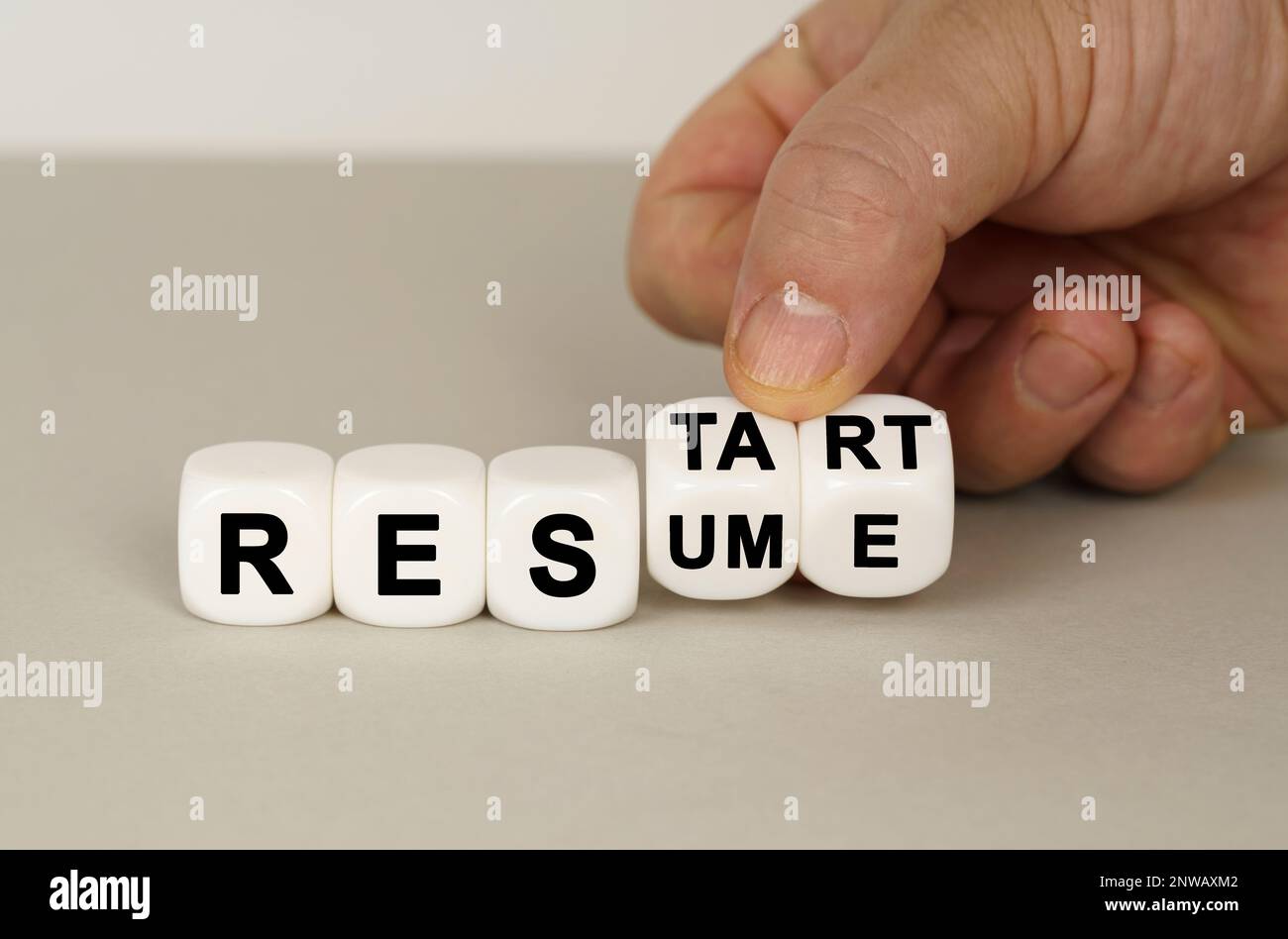 Su una superficie grigia sono presenti cubi bianchi con l'iscrizione - RIAVVIARE o RIPRENDERE. Due dadi in mano. Concetto aziendale. Foto Stock