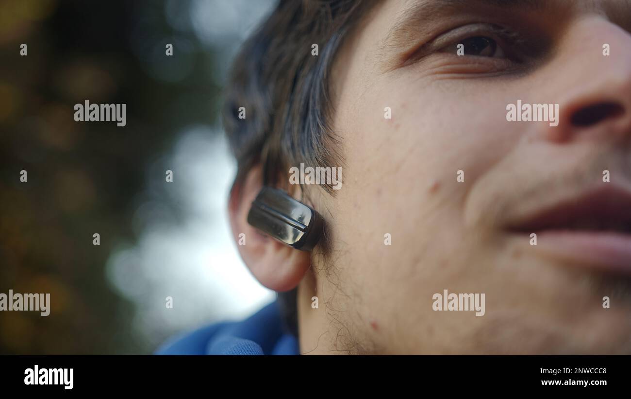 Primo piano di un giovane uomo sorridente che indossa auricolari Bluetooth che ascolta la musica Foto Stock