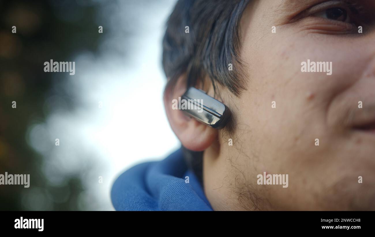 Giovane uomo sorridente che indossa gli auricolari Bluetooth che ascoltano la musica Foto Stock