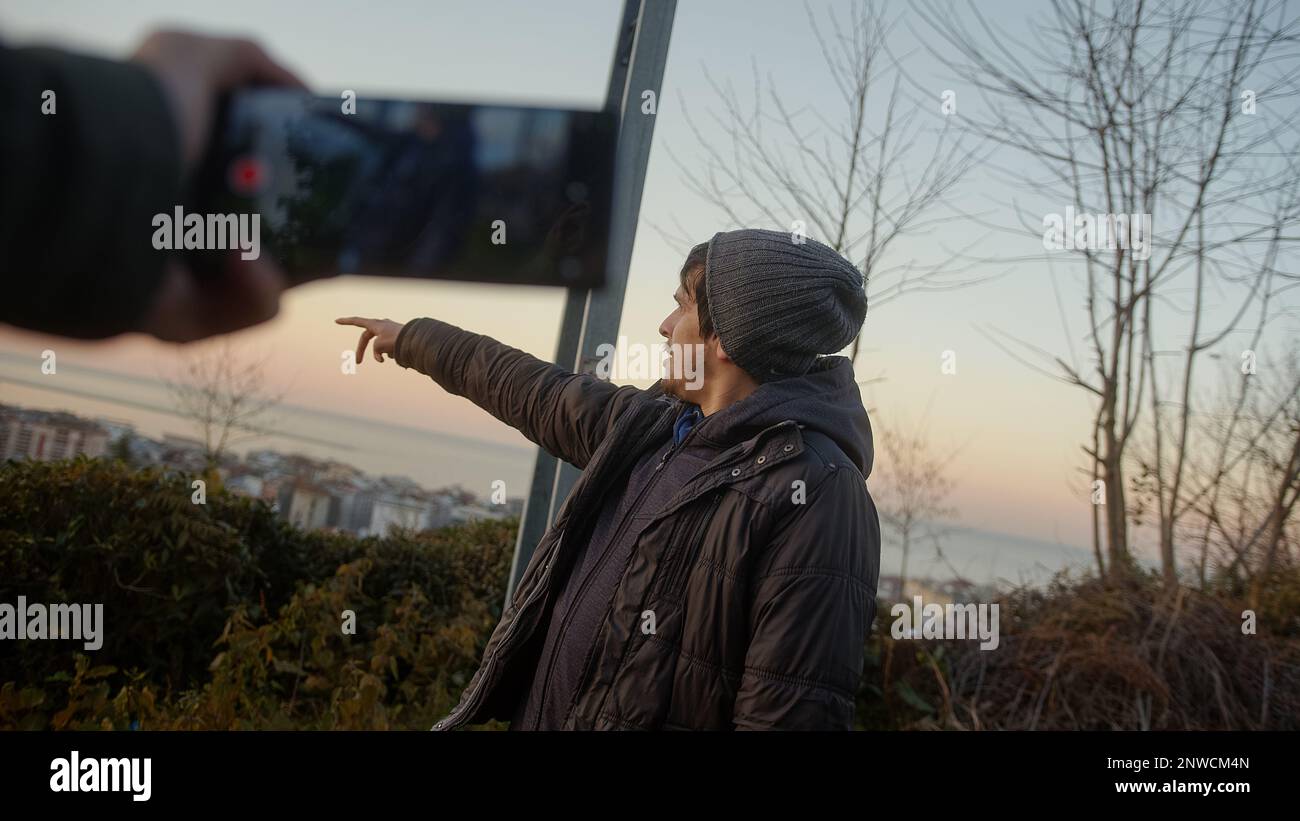 Maschio Influencer cattura video con il telefono in campo verde bello durante il tramonto stupefacente in natura Foto Stock