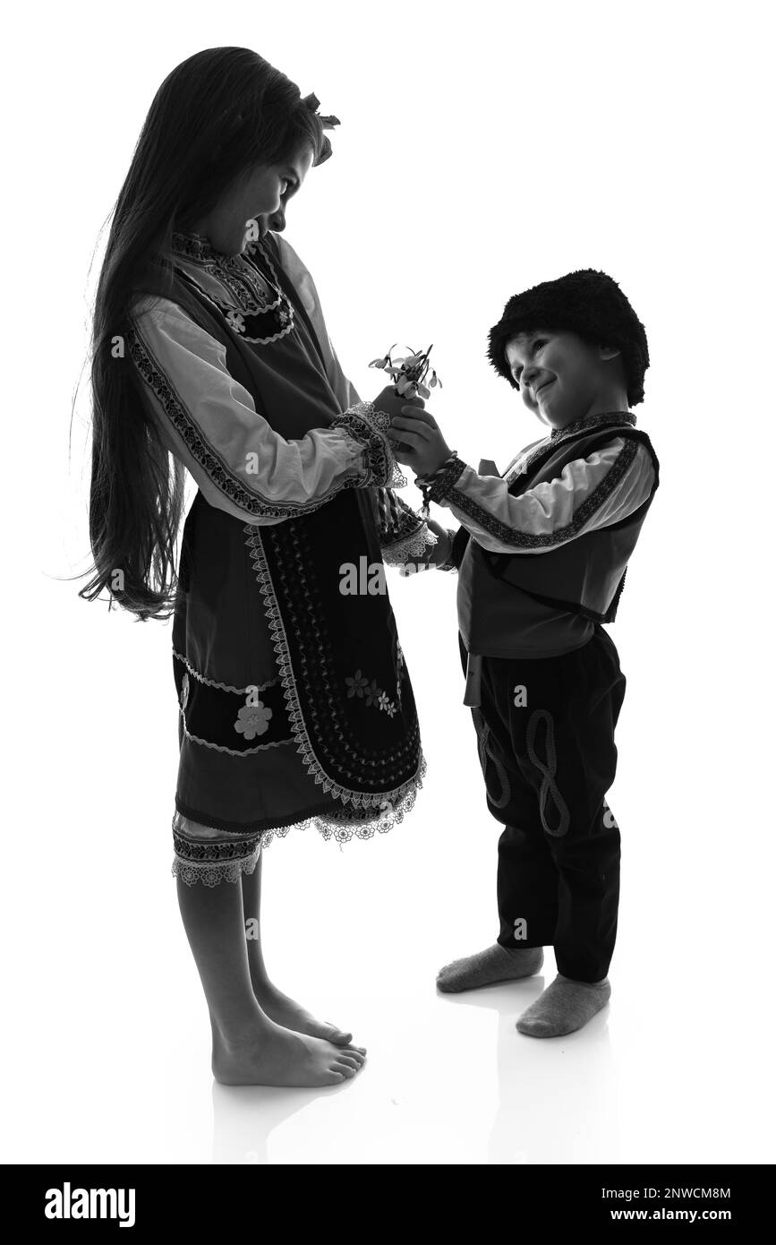 Ragazzo bulgaro, ragazza in costumi etnici folcloristici, mazzo di fiori primaverili nevicate, martenitsa di lana simbolo di marzo Baba Marta vacanza, Bulgaria Foto Stock