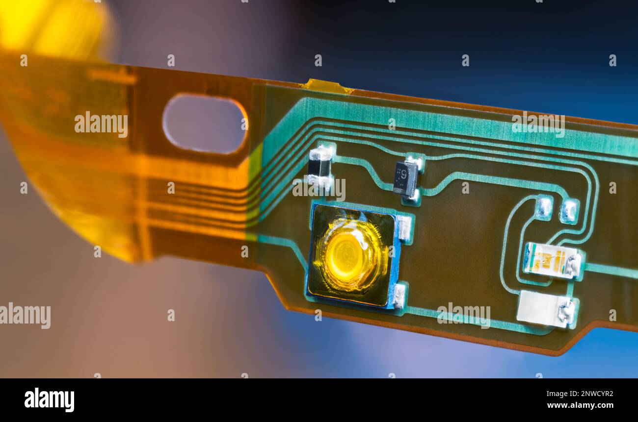 Striscia in plastica di componenti elettronici a montaggio superficiale e circuiti stampati flessibili. Primo piano di linee verdi e gialle su PCB smontata di cuffie. Foto Stock